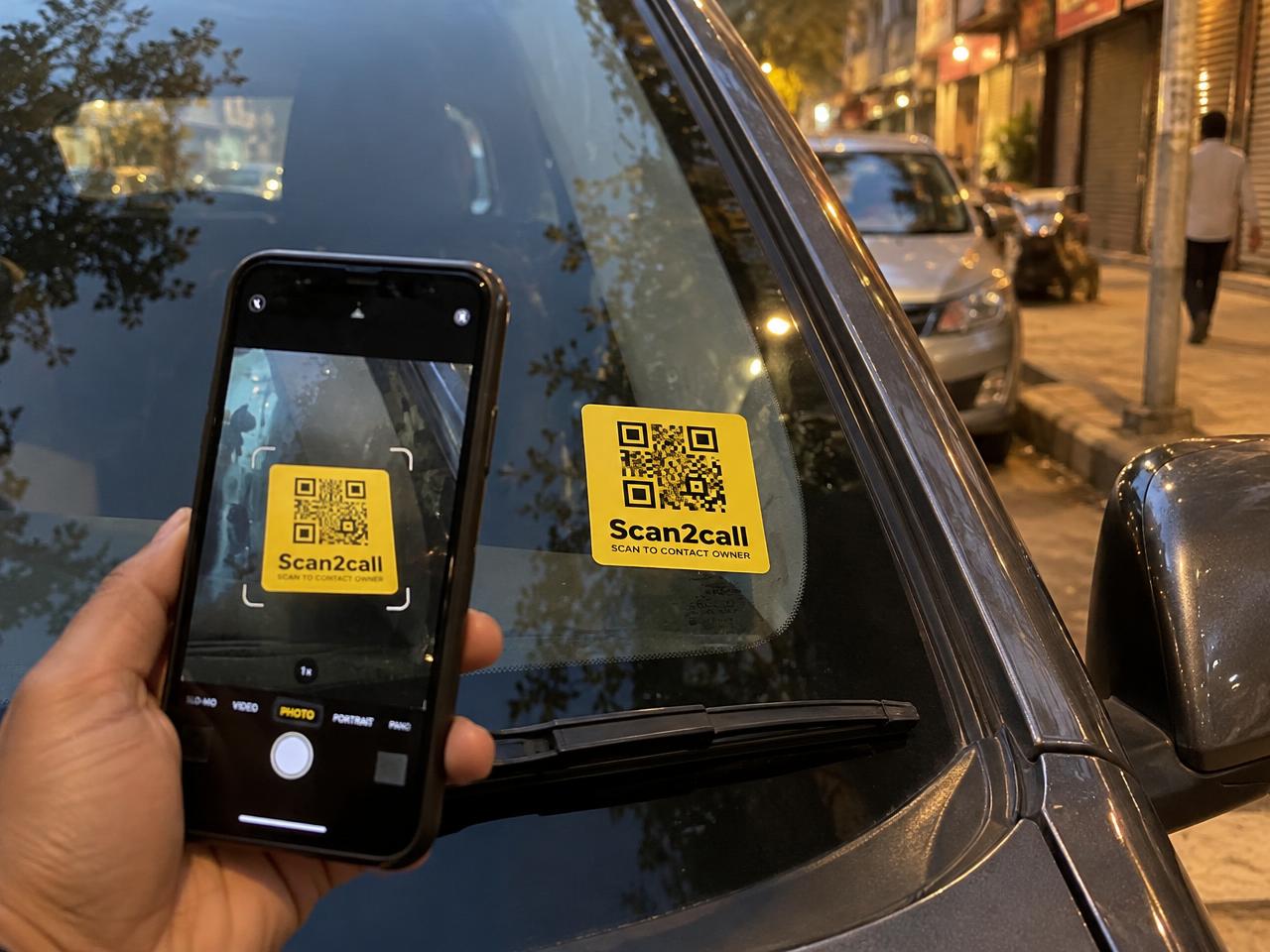 Someone scanning a Scan2call QR sticker on a car windshield with their phone